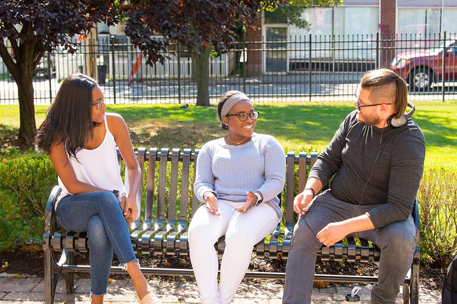 Three Iona students sit on a bench outside of the library.