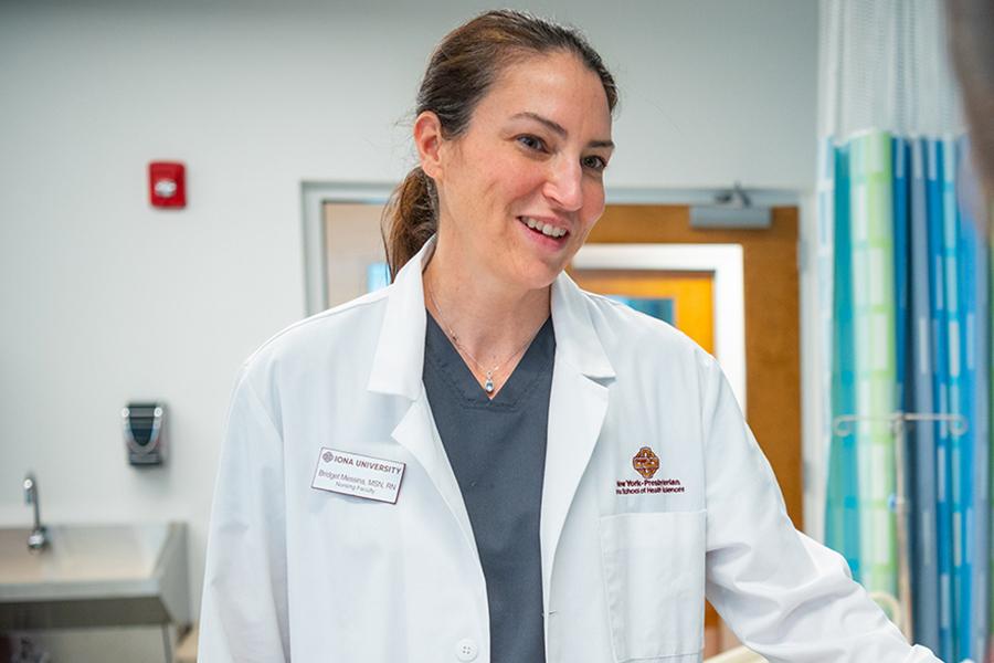 A nursing professor in a white lab coat smiles and helps a student.