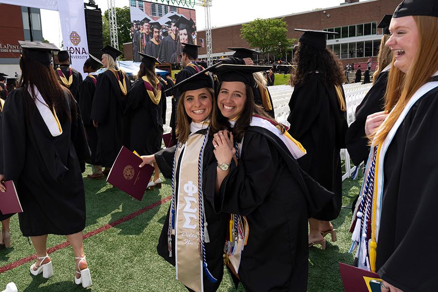Two 2023 graduates smile at the Commencement ceremony.
