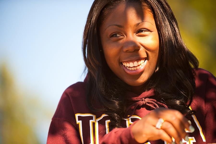 A student in an Iona sweatshirt smiles on a sunny day.