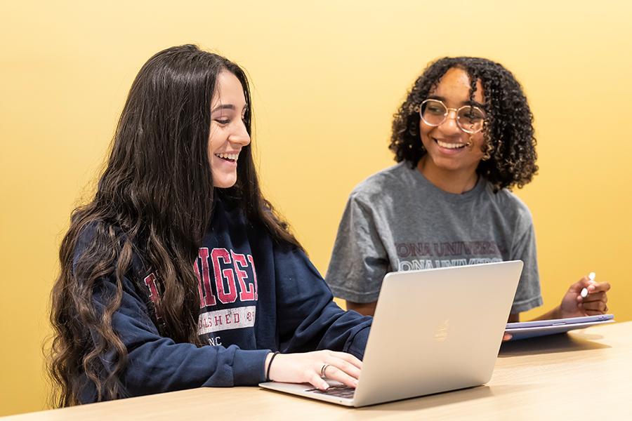 Two students work on a laptop in the LaPenta School of Business and smile.