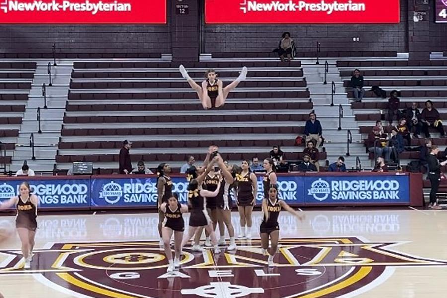 The cheer team makes a pyramid and a member jumps high in the air for them to catch.