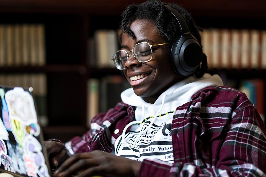 A student with headphones works on a laptop and smiles.