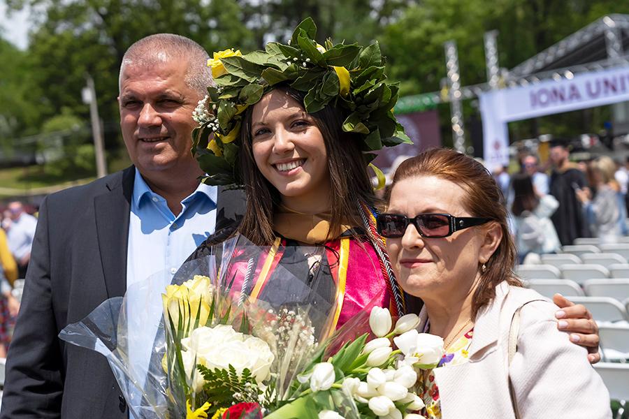 A graduate with flowers on her cap poses with her parents at Commencement.