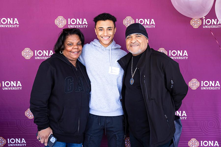 A student smiles with his parents in front of the step and repeat.