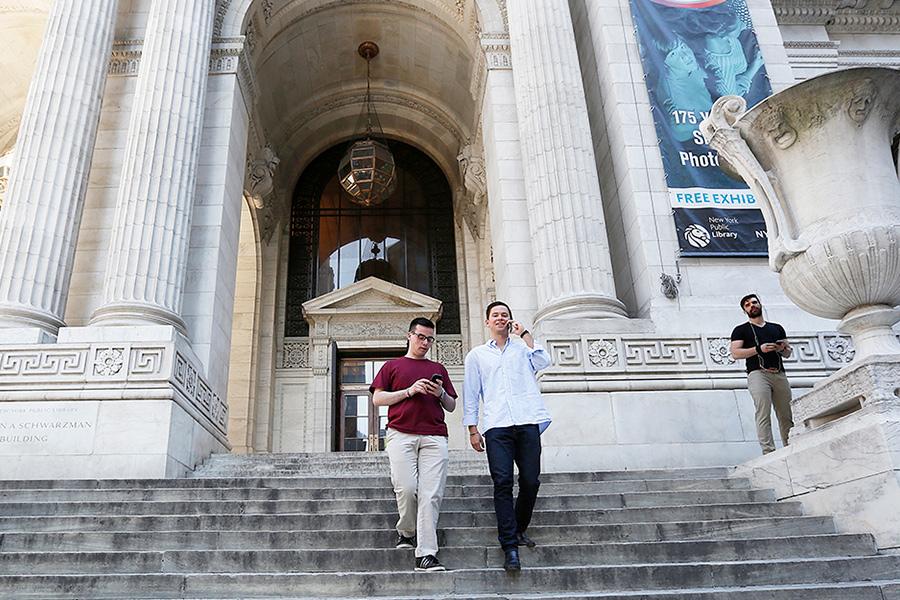 Two students walk down the steps of the NYC public library.