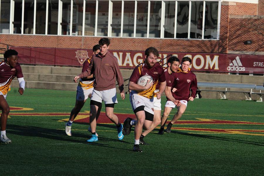 A rugby player running downfield with the ball.