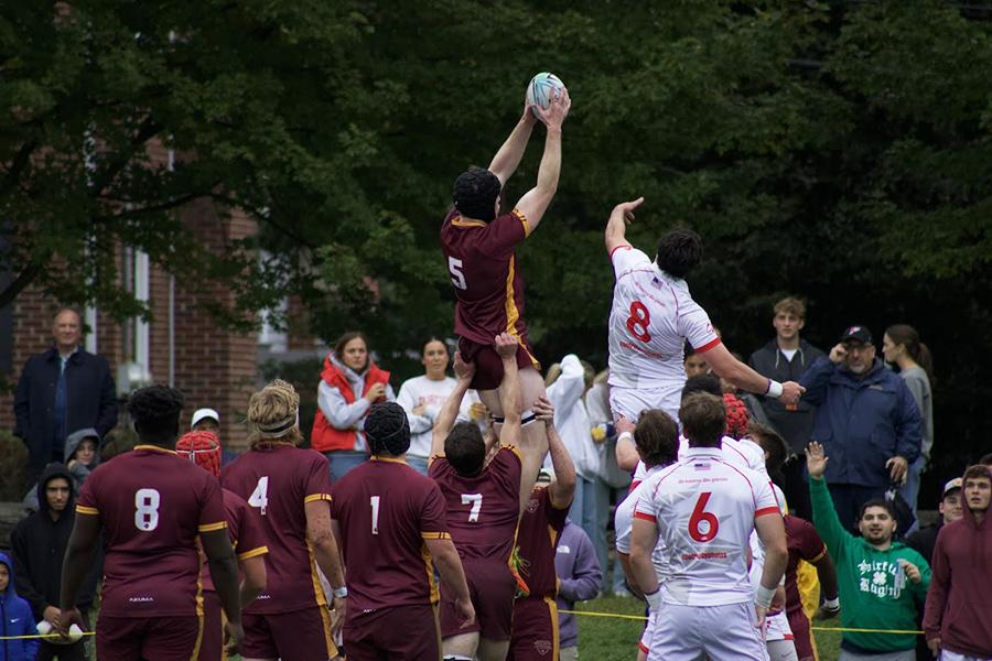 The rugby team during a game where the player is up in the air catching the ball.