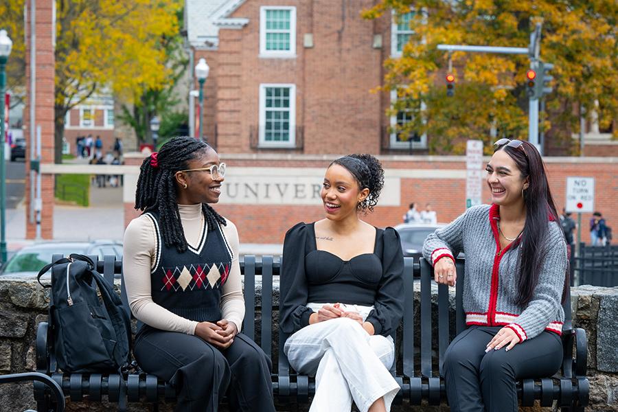 Three school psychology students sit on a bench and talk and smile.