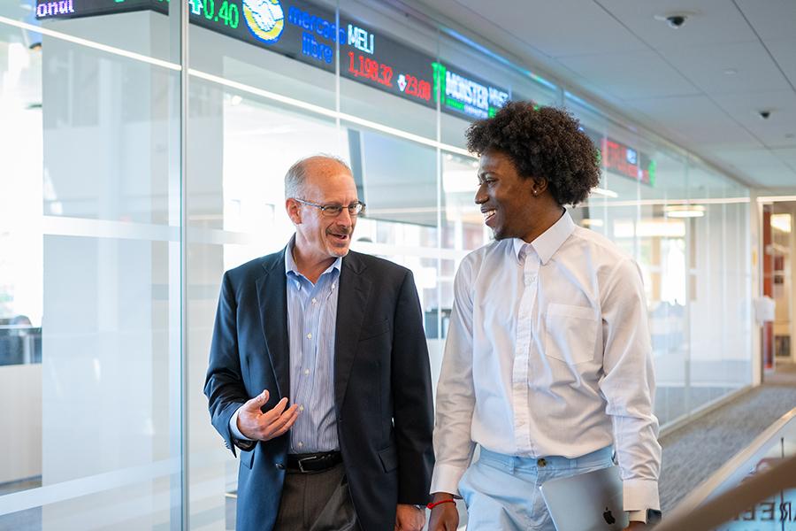 A student and professor walk down a hallway by the ticker room.