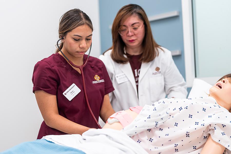 A nursing student works with a professor on a mannequin.