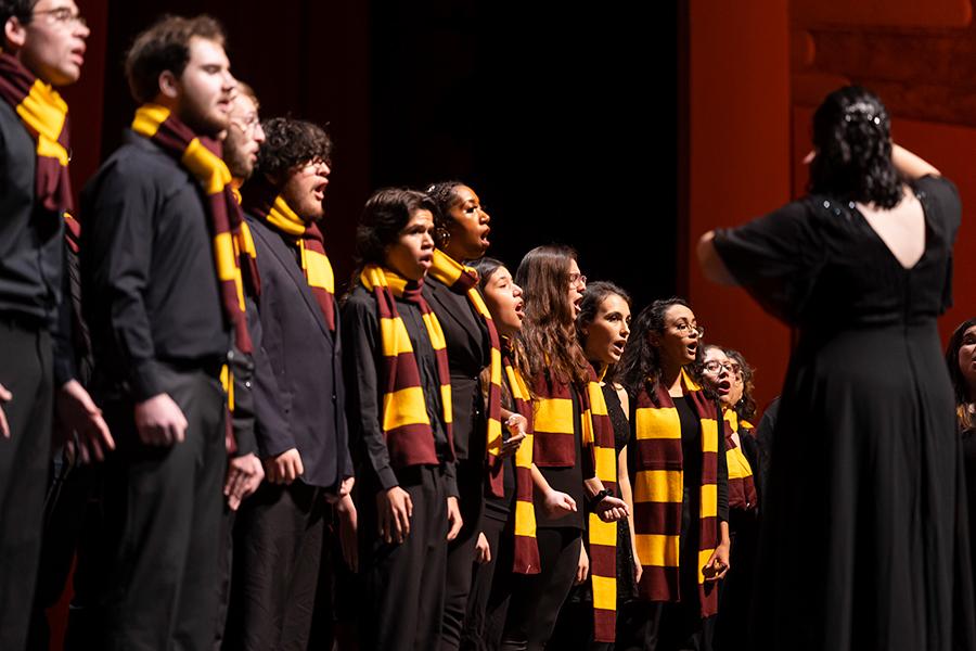 The singers perform at Radio City Music Hall with matching maroon and gold scarves.