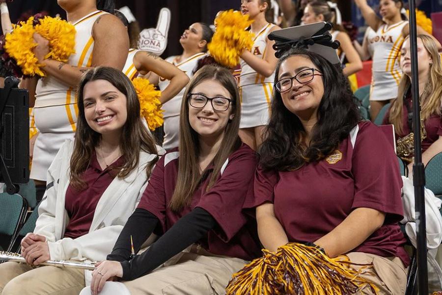 Three pep band members smile at a basketball game.