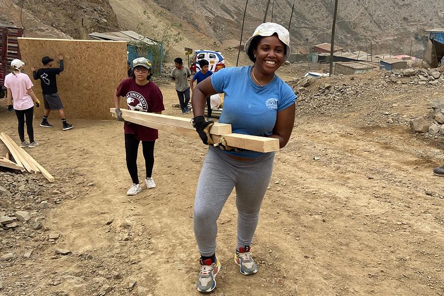 Students carry lumber up a hill in Peru to help build a house.