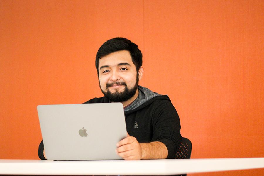 A student works on his laptop in a study room and smiles.