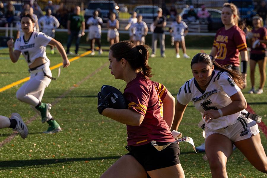 Iona University's Women's Club Flag Football player running with the football avoiding the opposing team.