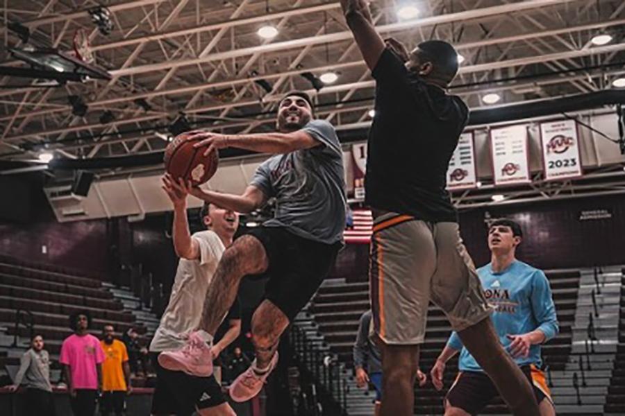 An intramural basketball player, mid air, trying to score a lay up with two defenders on each side.