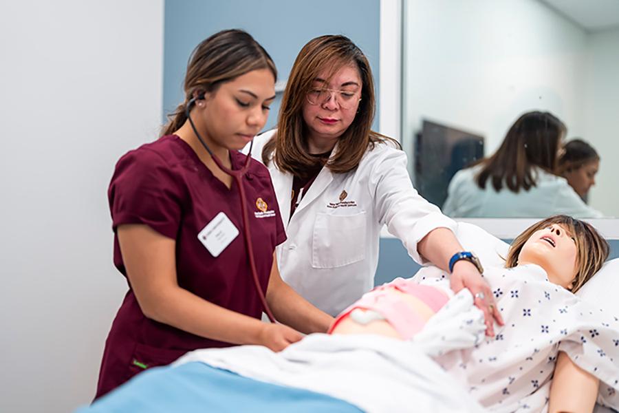 A professor and a nursing student practice on a mannequin.