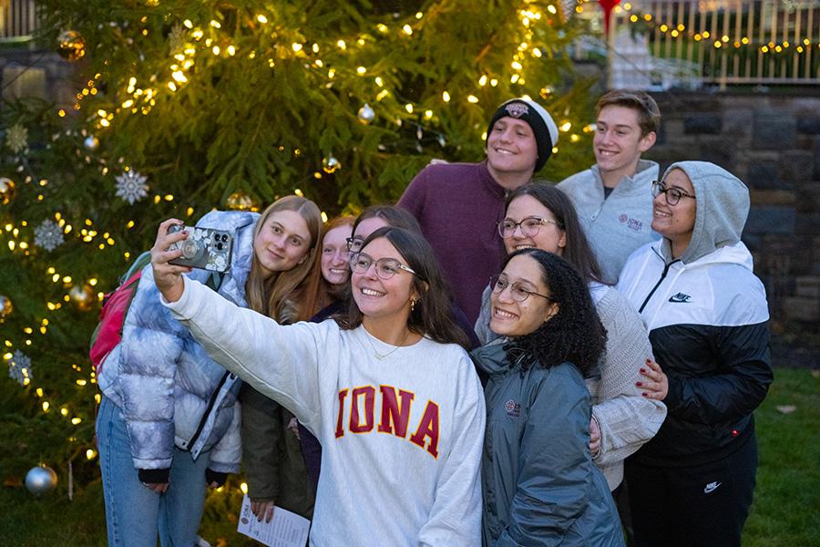 A group of students take a selfie in front of the Christmas tree. 