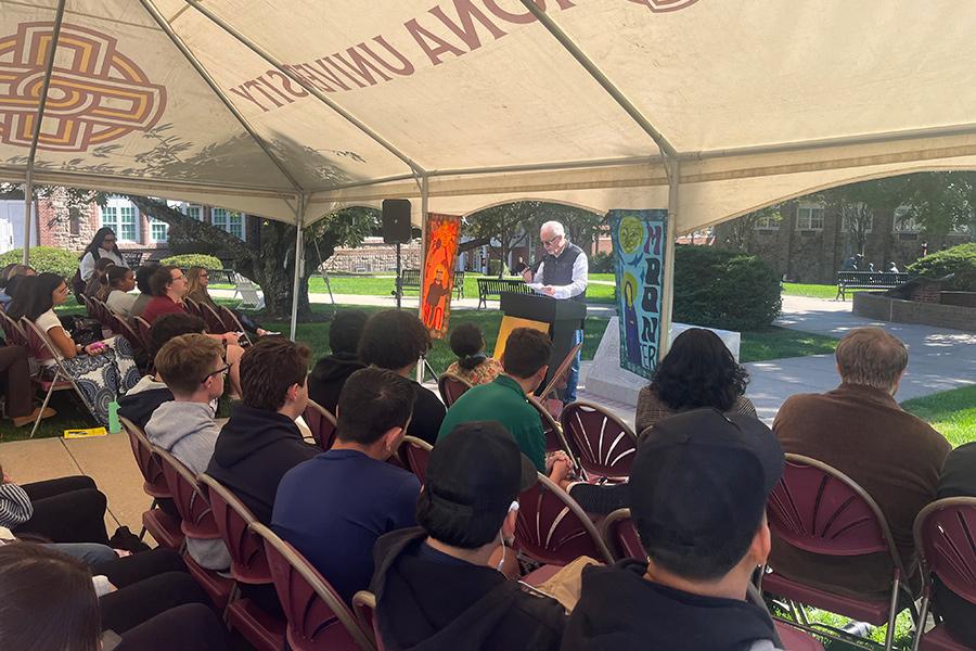 An event being held on the Iona University New Rochelle Campus, celebrating and recognizing Jidapha Vastola ’27 art mural banners with a guest speaker at the podium and the crowd is seated.