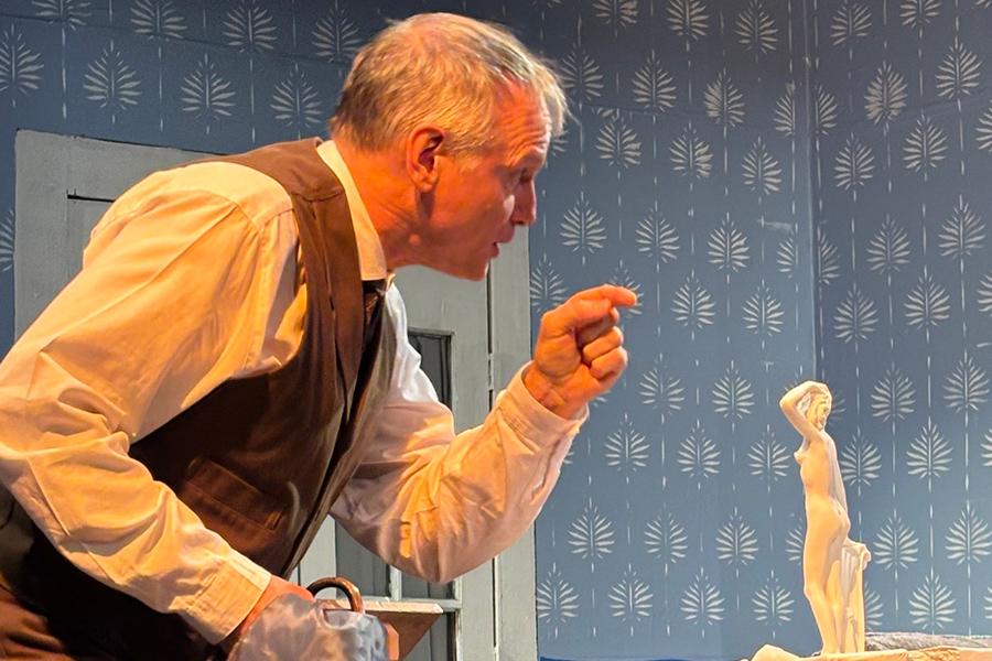 A male actor crouching, pointing with his left arm, and speaking on stage during the play "Creditors."