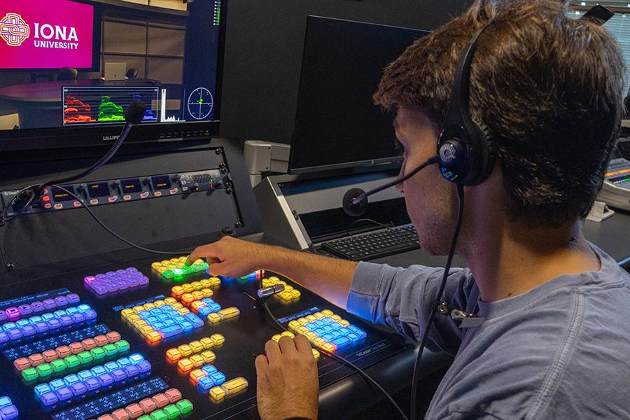 A male student sitting in the soundboard room, working and pressing buttons on the soundboard.