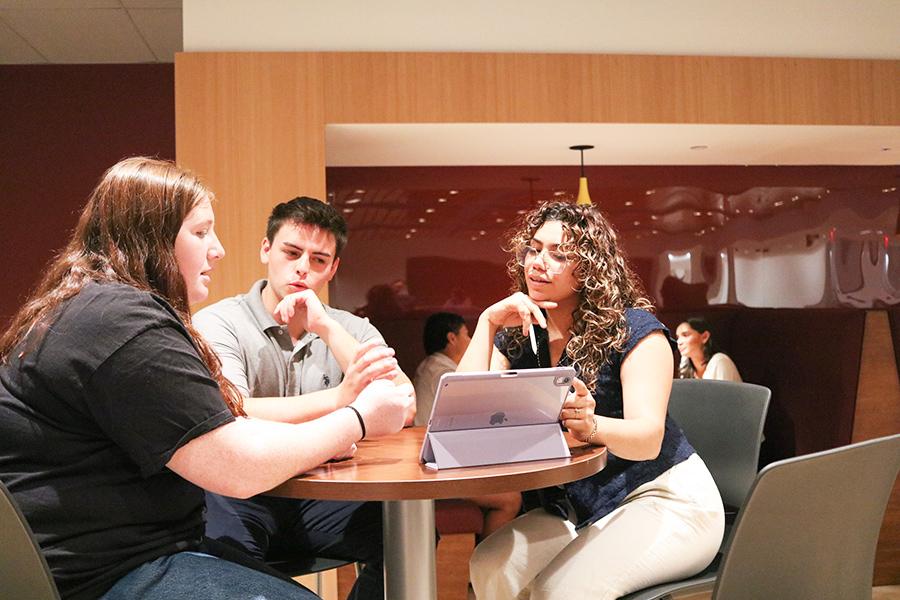 Three students work at a laptop together in the lounge.
