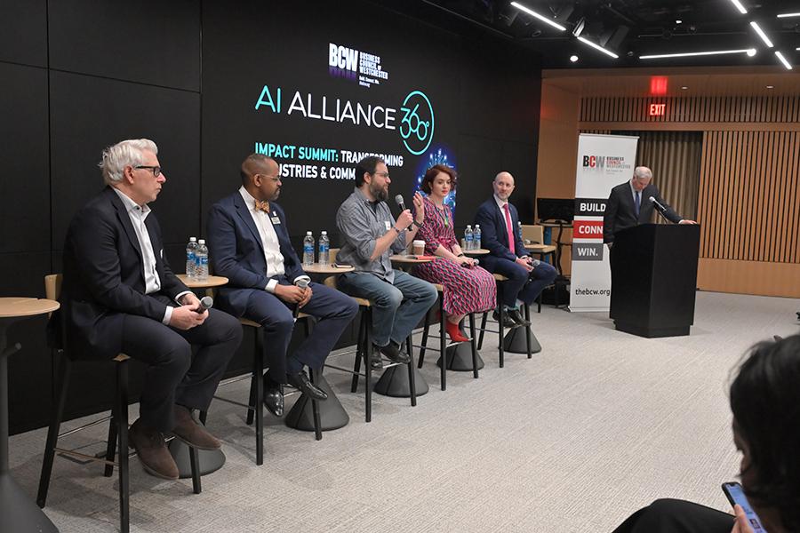 Five panelists sit on high stools in front of a digital stage backdrop while Iona University’s Rob Kissner speaks into a microphone.