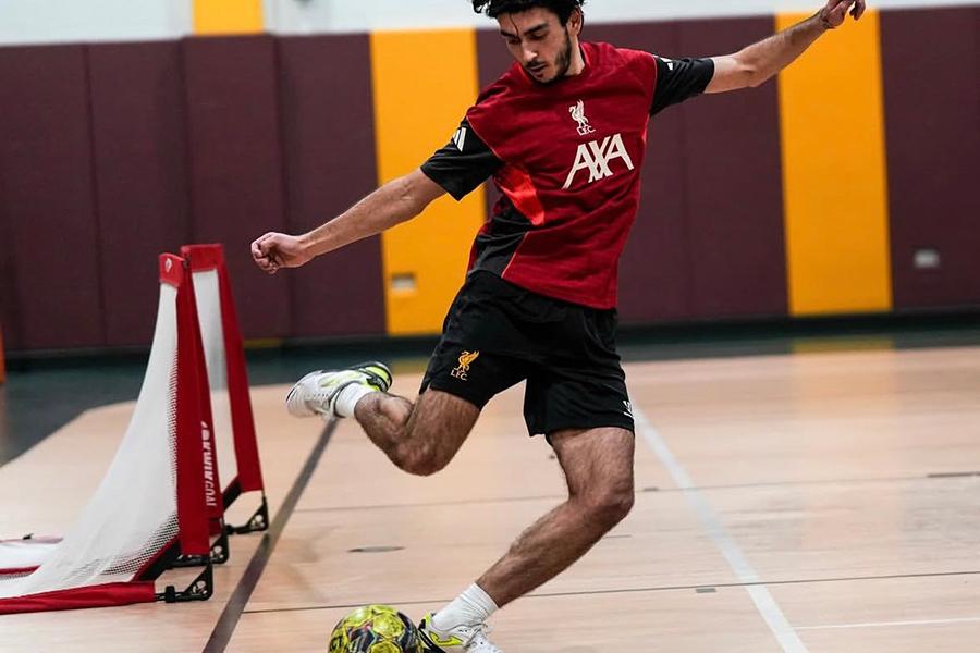 An intramural soccer player is kicking the ball away from the goal.
