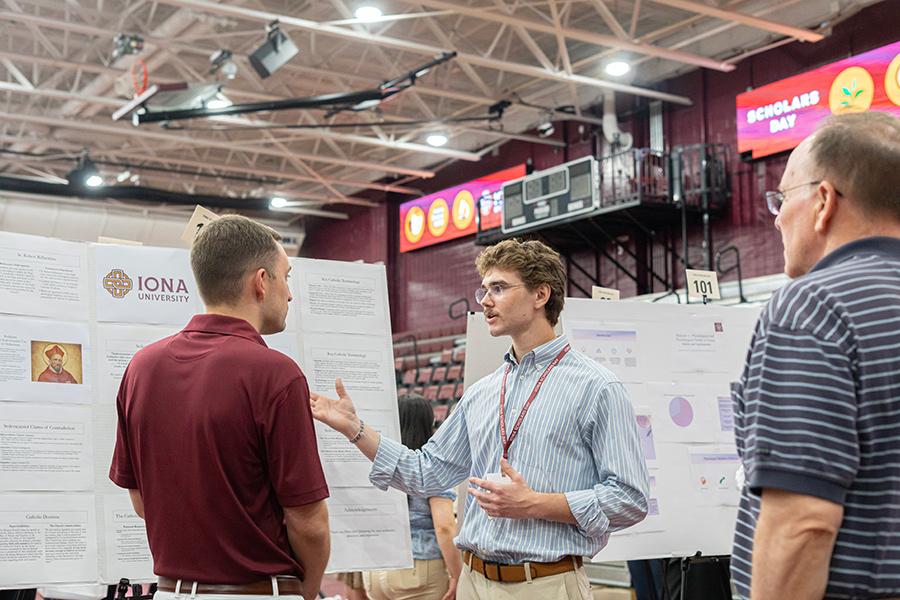 A student presenter explaining and discussing his research poster board at Iona Scholars Day.