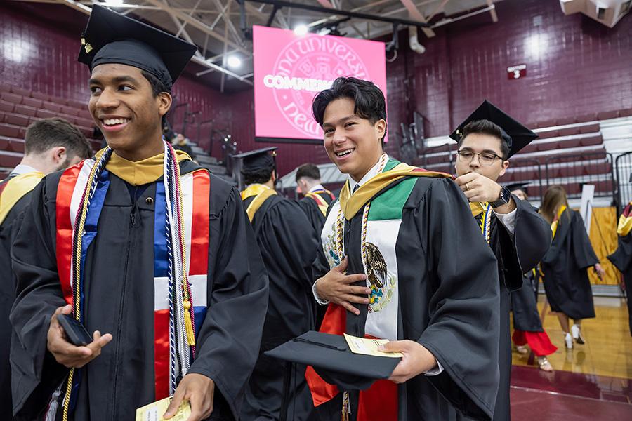 Three graduates help each other prepare for Commencement.