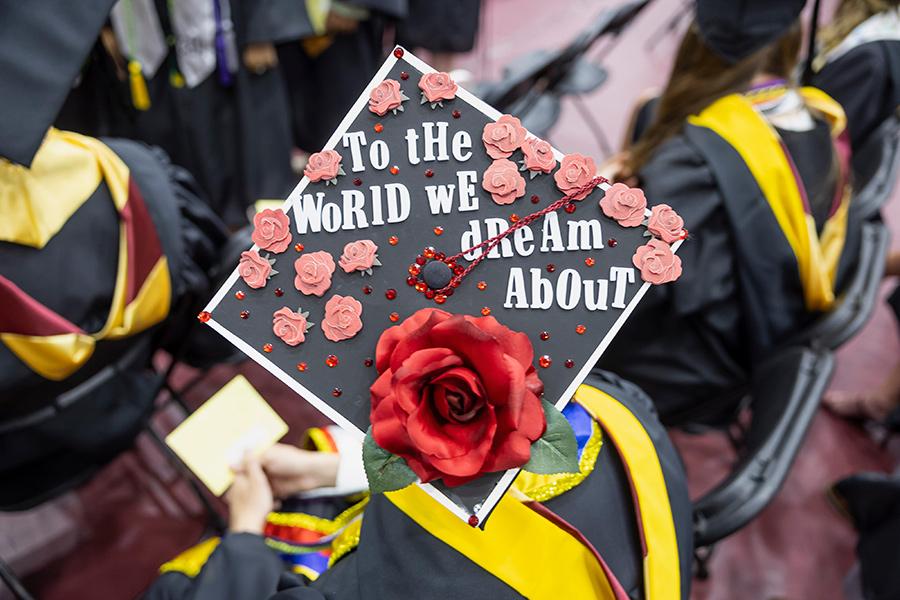 A graduate's decorated cap reads "To the world we dream about."