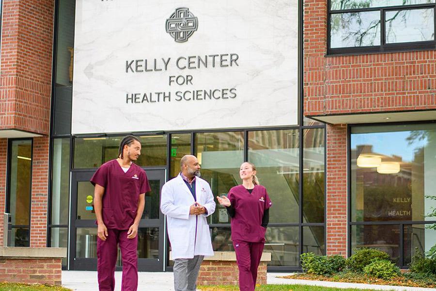 A professor and two students walking outside of the Kelly Center for Health Sciences.