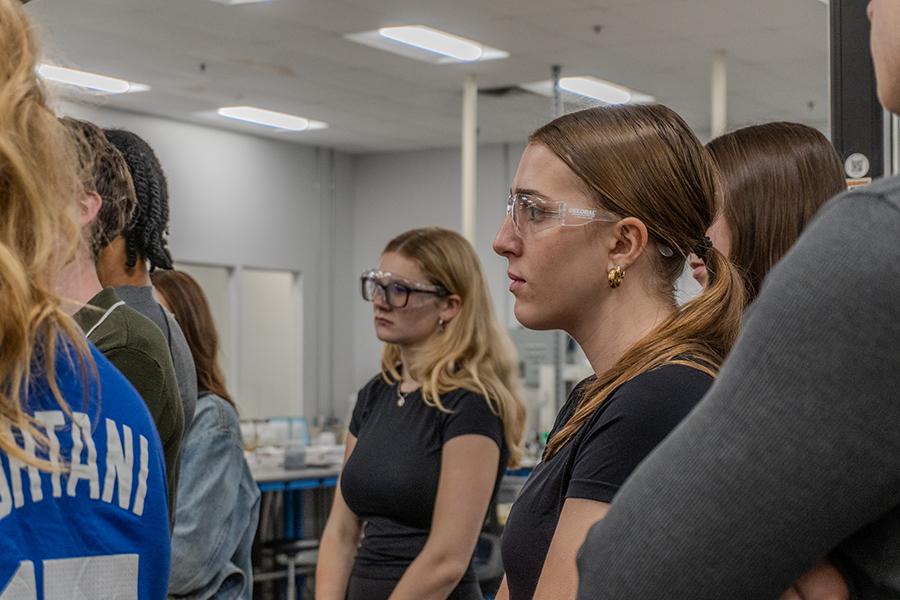 Students wearing safety glasses and listening closely during a tour of the laboratory facility at Eos Energy Enterprises.