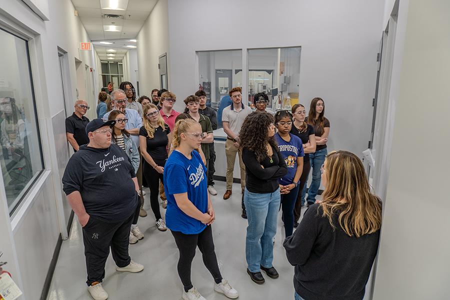 A large group of Iona University students wearing safety glasses while listening to a guide in a hallway during their tour of the Eos Energy Enterprises facility.