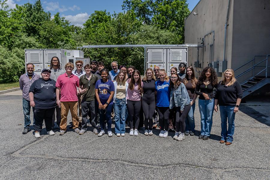 Iona University students and faculty smiling together while standing outside in front of industrial energy storage units during their tour of Eos Energy Enterprises.
