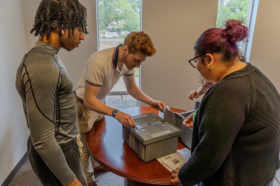 Three Iona University students gathered around a table to closely examine a specialized equipment container during their tour of Eos Energy Enterprises.