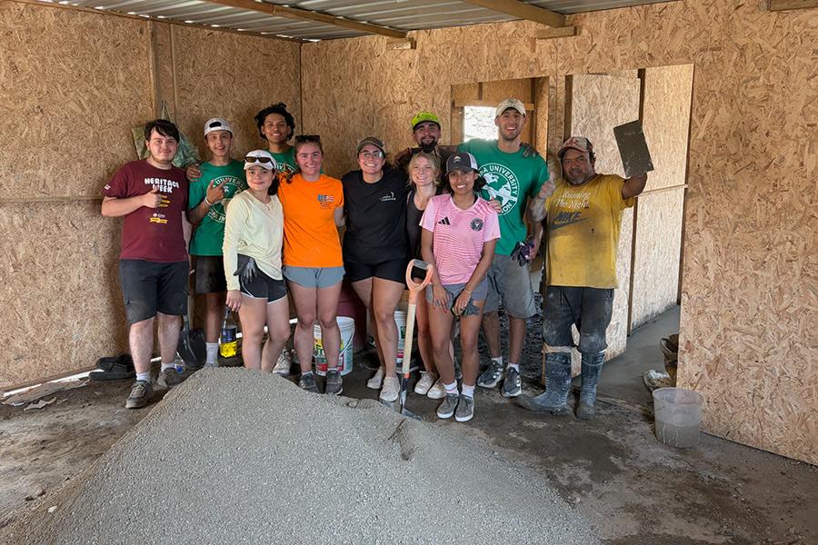 A large group of students and local workers smiling together inside a building under construction on an Iona University immersion trip.