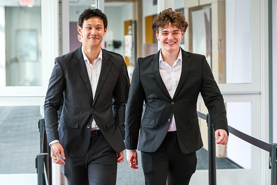 Two sales minors in suits walk down the hallway. 