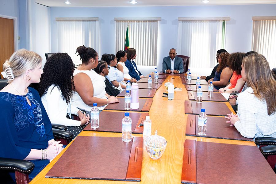 A group of students and program leaders seated along a long conference table during a meeting with Prime Minister Roosevelt Skerrit of Dominica.