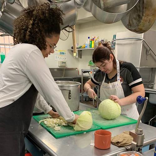 Two students from Mission and Ministry volunteer in a kitchen.