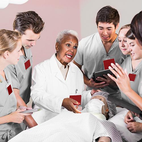 A nursing professor instructs a group of nursing students using an artificial patient doll.