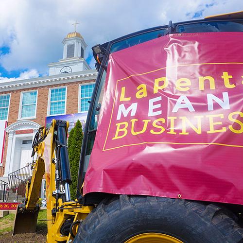 A backhoe with a tarp that reads LaPenta Means Business at the groundbreaking ceremony.