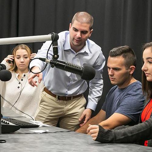 Joe from Media & Strategic Communication department shows three students how to use the podcast/radio equipment.
