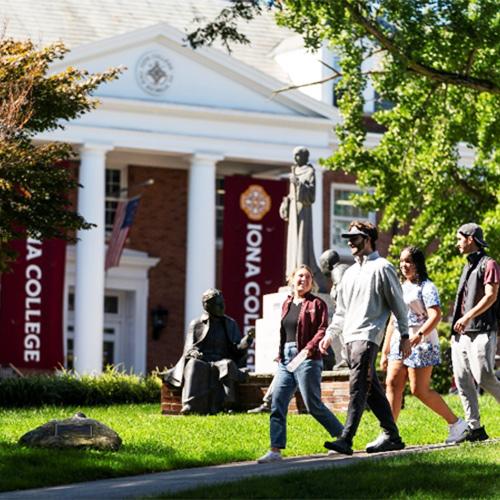 Four students walk in front of McSpedon Hall on a sunny day.