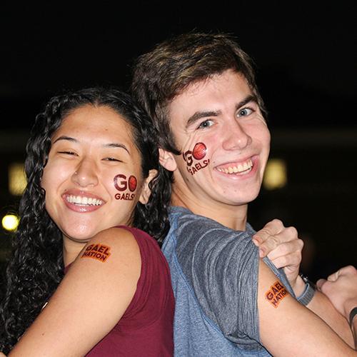 Two students smile and show off their Go Gaels tattoos.