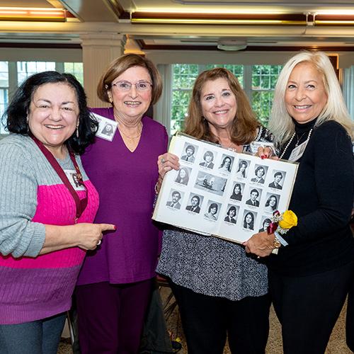 Four friends of the class of 1973 smile and hold their yearbook.