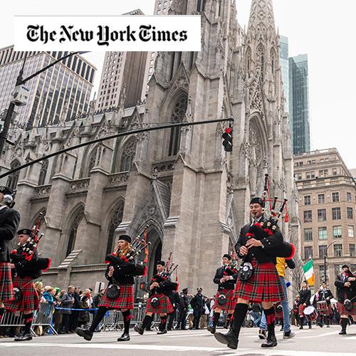 The pipers march in the St. Patrick's Day parade with the NY Times logo.