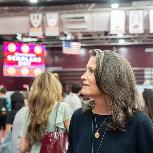 Amy Emmerich ’97 smiles while looking toward student presentations during Iona Scholars Day with a digital event sign visible in the background.