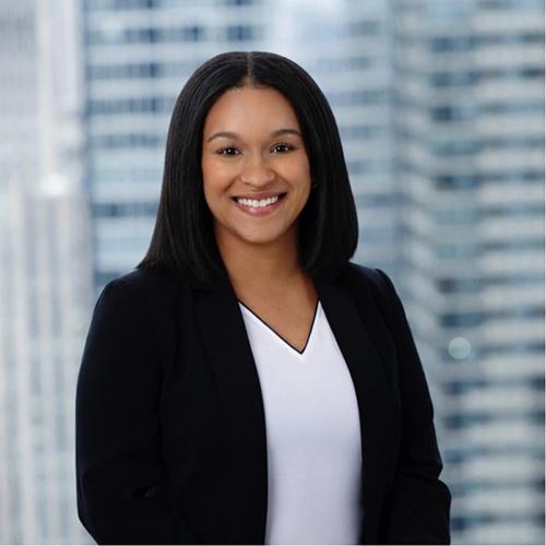 A professional headshot of Lucille Bootman smiling in a black blazer and white top, set against a softly blurred background of city high-rises.